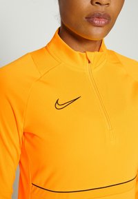 Sudadera Nike en naranja brillante, con cremallera en la parte delantera a media altura, cuello alto y logotipo negro. Tejido suave y elástico con detalles en contraste.