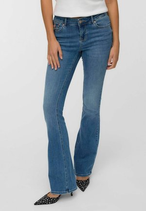 Flared blue denim jeans with a mid-rise waist, classic five-pocket design, and subtle fading, paired with black polka-dot pointed heels.