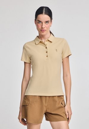 Beige Polohemd mit Kragen und kurzen Ärmeln, ausgestattet mit fünf braunen Knöpfen und einem kleinen gestickten Logo im Brustbereich.