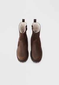 Botas de tobillo de cuero marrón con un suave forro de piel de oveja, paneles laterales elásticos y una lengüeta trasera para facilitar su puesta. Suela resistente para un mejor agarre.