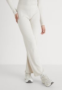 Ribbed, lys beige bukser med høj talje og bred ben-design, parret med grå sportsko, der har tekstureret stof.
