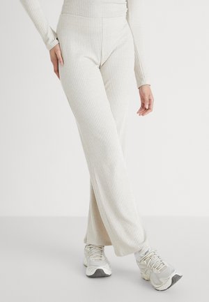 Pantalones acanalados de color beige claro con una cintura alta y un diseño de pierna ancha, combinados con zapatillas deportivas grises, con tejido texturizado.