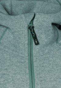 Ljust grå zip-up hoodie i mjukt stickat material med foder i huvan. Har kontrasterande grön dragkedja och sömdetaljer.