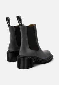 Botas de tobillo de cuero gris con paneles laterales elásticos, tacones de goma negra acanalada y lengüetas con el logo de la marca en la parte trasera.