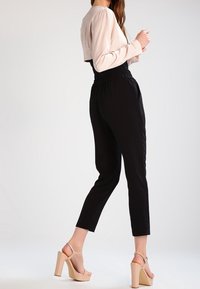 Black tapered trousers with an elastic waistband paired with a light pink long-sleeve top. Beige block-heeled sandals complete the outfit.