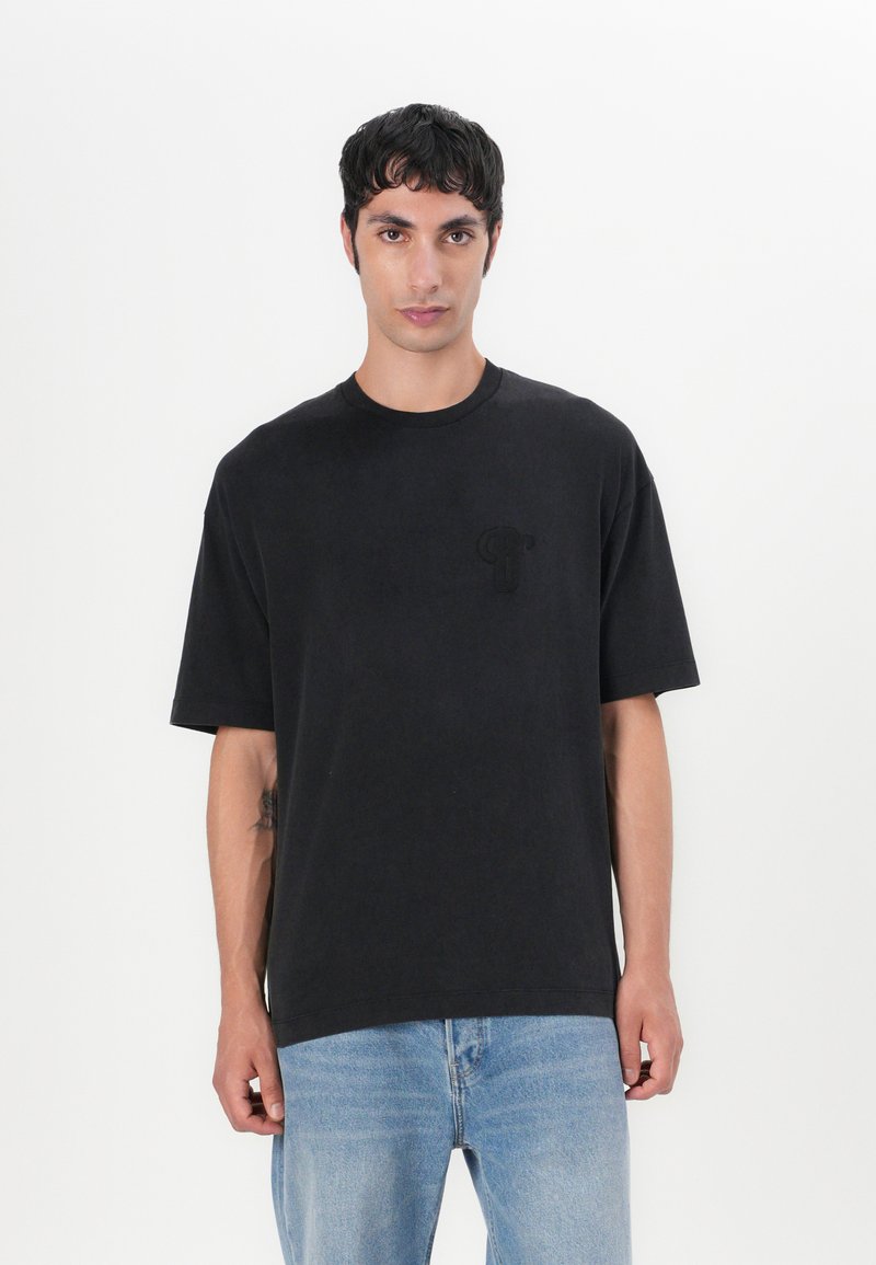 Schwarzes Baumwoll-T-Shirt mit Rundhalsausschnitt und kurzen Ärmeln. Hat ein dezentes Ton-in-Ton-Logo auf der linken Brust. Leicht entspannter Schnitt.