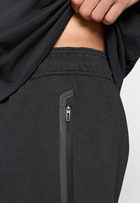 Μαύρα αθλητικά παντελόνια τζόγκερ με υφή, με ελαστική μέση και τσέπη με φερμουάρ με αντίθετες γκρι λεπτομέρειες.