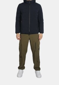 Giacca puffer blu navy con zip frontale, abbinata a pantaloni cargo color olivo con multiple tasche e sneakers bianche.