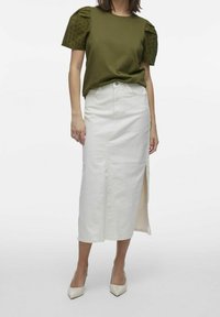 Olivgrön topp med spetsiga puffärmar, tillsammans med en vit knälång denimkjol med en sidoklyfta och klassiska klackskor.