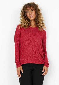 Rode longsleeve top van zacht, textuurstof met een losse pasvorm en een V-halslijn, gecombineerd met zwarte strakke broek.