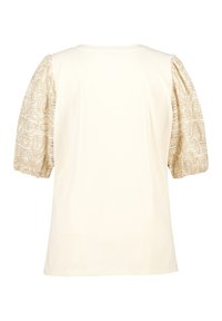 Crème-kleurige top met korte, opgeblazen mouwen van ingewikkeld patroon van beige kant. Basic ronde halslijn; soepele textuur.