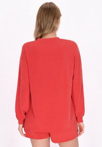 Rød ribbet sweater med lange ærmer, høj hals og afslappet pasform, parret med matchende shorts. Stoffet har en struktureret overflade.