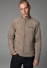 Chaqueta de ante topo con cuello alzado, cierre delantero de cremallera y bolsillo en el pecho con cremallera; presenta detalles de costura y bolsillos laterales.