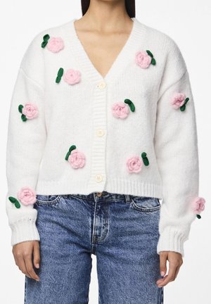 Cárdigan blanco de punto con apliques florales 3D en rosa y verde, con botones al frente, combinado con jeans de mezclilla azules.