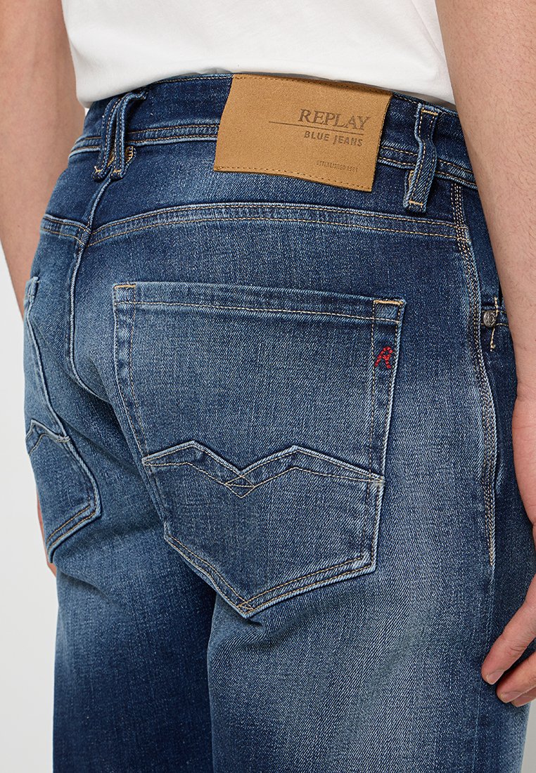 Blaue Jeans aus Denim mit einer verwaschenen Textur, ausgestattet mit einem taubengrauen Lederlabel am Bund und markanter Rückensteppung in Zickzackmuster.