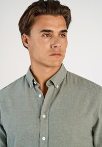 Jasnozielona koszula na guziki z kołnierzykiem, wykonana z teksturowanej tkaniny, z białymi guzikami i luźnym krojem.