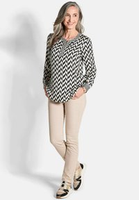 Blouse à manches longues avec un motif à chevrons noir et crème, associée à un pantalon beige et des baskets avec des accents noirs. Tissu doux, coupe décontractée.