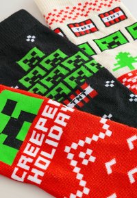 Drei Paare gestrickter Socken: schwarz mit pixelierten grünen Bäumen, cremefarben mit roten TNT-Mustern und rot mit weißem "CREEPER HOLIDAY"-Text.