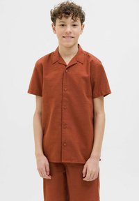 Korte mouw shirt in roestkleurige, gestructureerde stof met een kraag en knopen aan de voorkant. Gepaard met bijpassende shorts in hetzelfde materiaal.