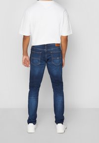Mörkblå denimjeans med slim fit, femfickorsdesign och ljusa sömnadsdetaljer. Matchad med en enkel vit t-shirt och vita skor.