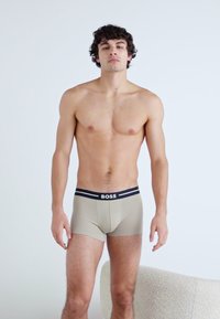 Beige boxer alsónadrág fekete derékszíjjal, amelyen a "BOSS" márkaneve látható. Az anyaga sima, testhezálló kialakítással.