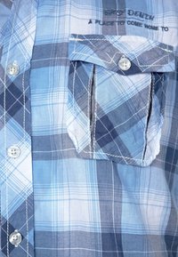 Camicia a quadri blu e bianca realizzata in cotone leggero. Presenta una tasca sul petto, chiusura con bottoni e cuciture a contrasto.