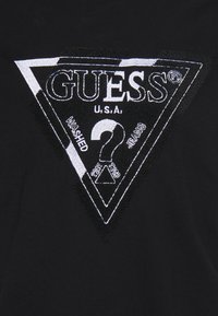 Sort bomulds t-shirt med et trekantet broderet logo. Logoet inkluderer ordet "GUESS," "U.S.A.," og tal, med hvide accenter.