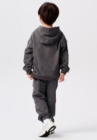 Grijze hoodie en bijpassende joggingsbroek, gemaakt van zachte stof. Heeft geribde manchetten en een tailleband, met sportieve witte en grijze sneakers.