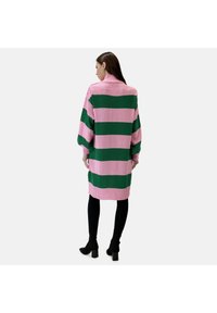 Vestido de punto con rayas horizontales en rosa y verde, mangas largas, un cuello alto y un corte relajado, combinado con leggins negros y botas de tacón.