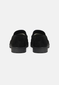 Chaussures en daim noir présentant une texture lisse, des bords arrondis et une semelle en caoutchouc profil bas avec un motif de semelle, vues de l'arrière.