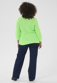 Lichtgroen, gestructureerd gebreid sweater met een ruitpatroon en driekwartmouwen, gecombineerd met donkerblauwe wijde jeans.