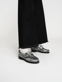 Silberne Lederschuhe mit Schnürsenkeln, die eine strukturierte Oberfläche und eine schwarze Gummisohle aufweisen. Kombiniert mit weißen Socken und schwarzen weit geschnittenen Jeans.