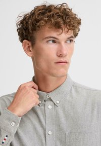 Grå knapper-up skjorte med teksturert stoff, med krage og lommepassasje. Knappe detaljer og en stripet aksent på mansjetten.