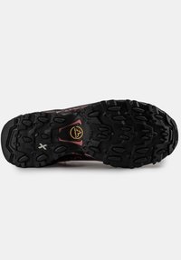 Černá gumová podrážka s hlubokými drážkami a několika protiskluzovými výstupky. Obsahuje růžový akcent a branding umístěný uprostřed.