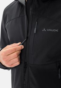 Giacca softshell nera con chiusura a zip, tasche per le mani e logo. Caratterizzata da una superficie liscia, zippature regolabili e fodera interna grigia.