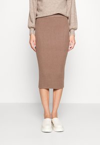 Ribbad stickad midiklänning i brun, med en figurnära form och elastisk midja. Matchad med lätta vita tofflor.