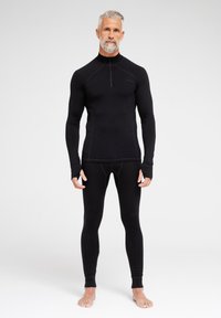 Schwarzes Thermaloberteil mit hohem Kragen und Viertelreißverschluss, kombiniert mit enganliegenden schwarzen Leggings. Glatte Textur, lange Ärmel mit Daumenlöchern.