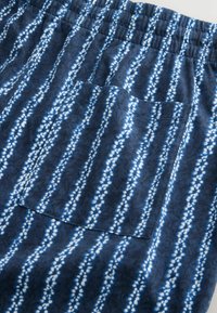 Tessuto blu scuro con strisce verticali bianche punteggiate e tasca a toppa quadrata, caratterizzato da una vita elasticizzata arricciata.