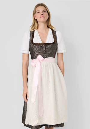 Frau trägt ein traditionelles braunes Dirndl mit Muster, einer weißen Bluse und einem hellrosa Band, das um die Taille gebunden ist.