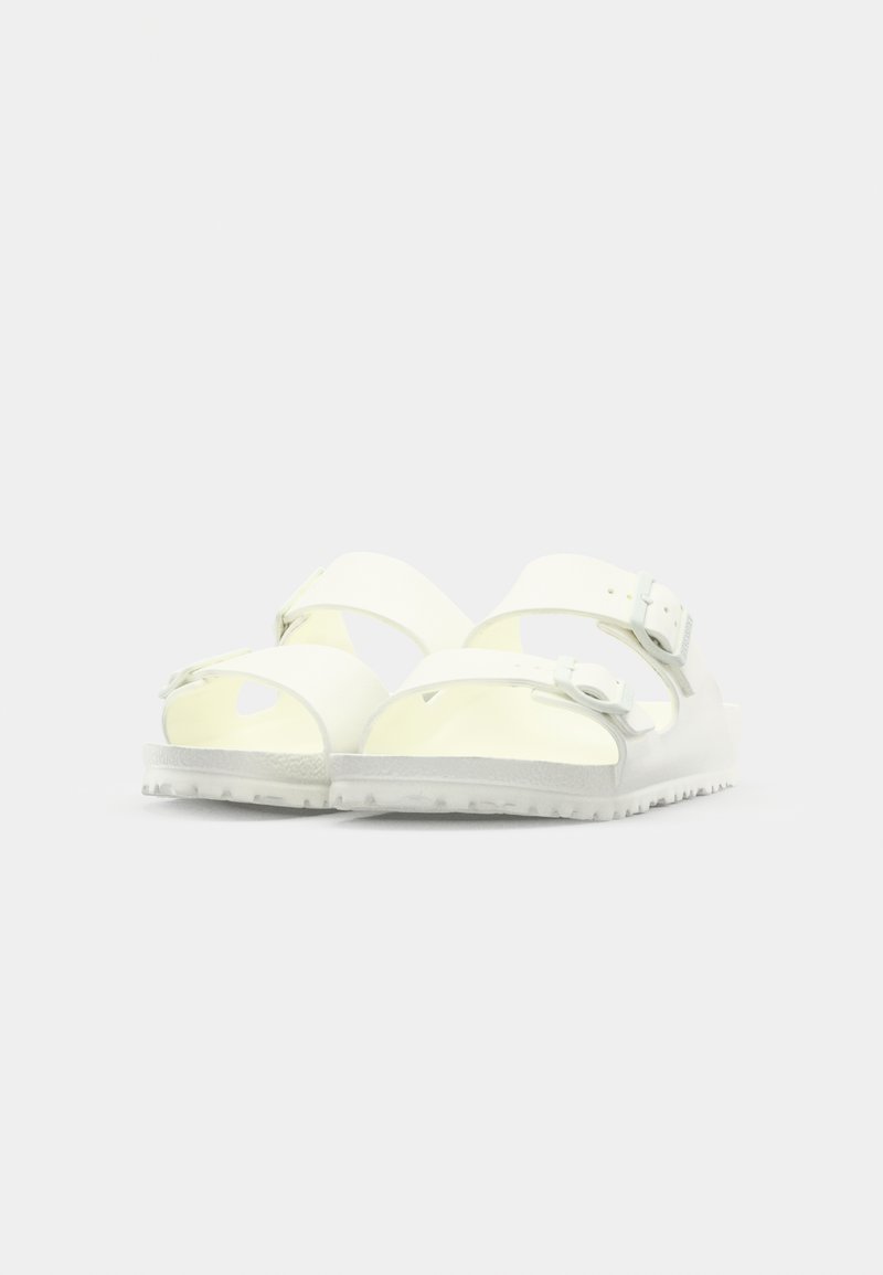 Sandalias blancas con dos correas ajustables, hechas de un material brillante. Suela blanca con dibujo y aberturas de ventilación en los laterales.