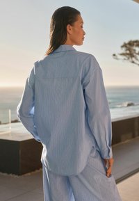 Camicia a righe blu chiaro con maniche lunghe e orlo curvo, realizzata in tessuto morbido, dotata di colletto a punta e leggera lucentezza.