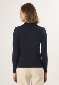 Navyblauwe, aansluitende trui met lange mouwen, geribbelde manchetten en een rode accent aan de onderrand. Glad textuur met een ronde kraag.
