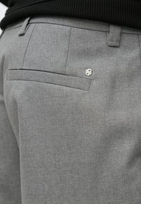 Szare teksturowane spodnie o wąskim kroju, z subtelną tylnią kieszenią oraz małym metalowym logo przy pasku.