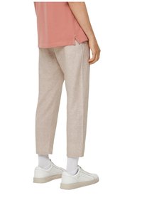 Person wearing beige cropped pants, white socks, white sneakers, and a salmon-colored shirt, shown from the back waist down.