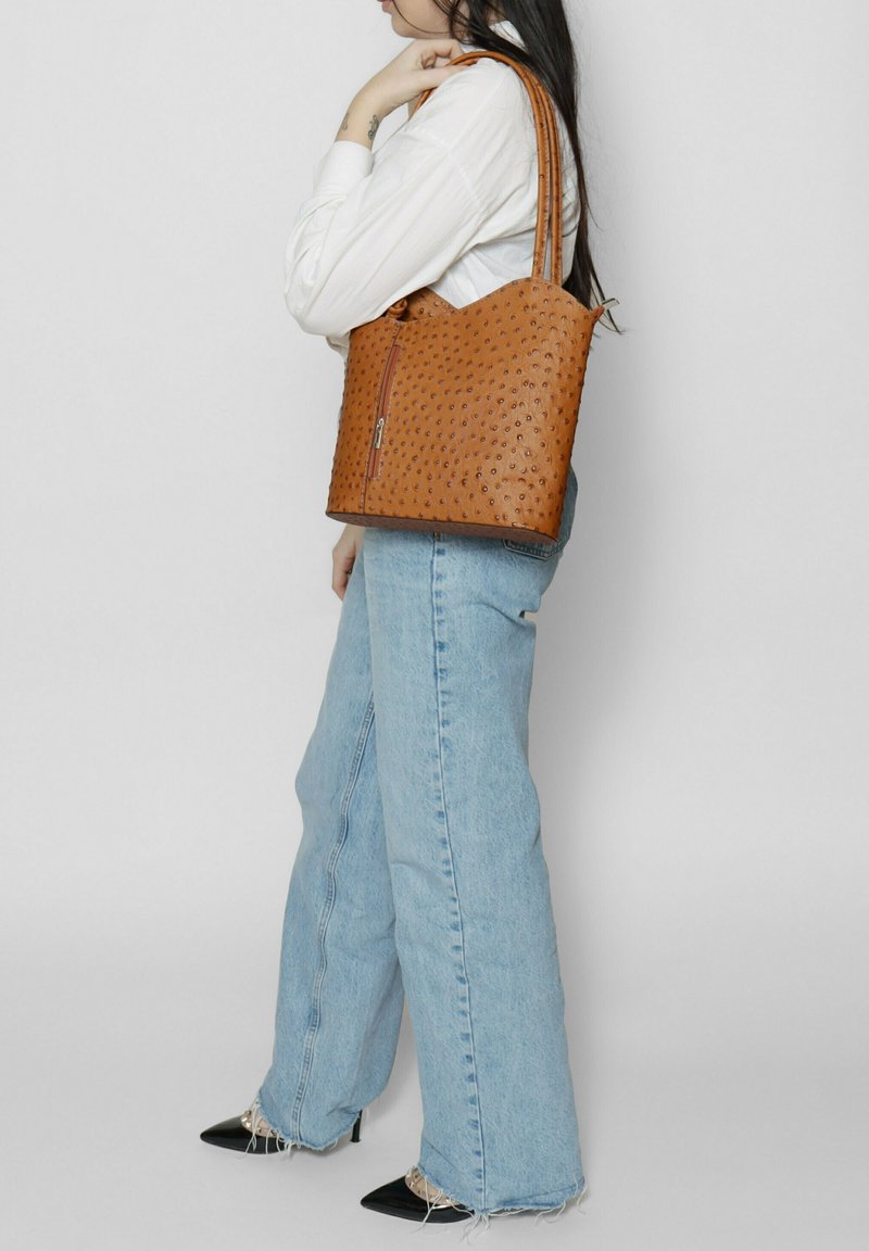 Borsa a tracolla in pelle marrone con motivo testurizzato, chiusura con zip e manici doppi. Abbbinata a jeans a gamba larga blu chiaro e scarpe nere con punta. 