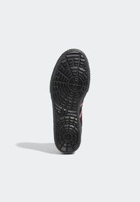 Suela de zapatilla negra con patrón de agarre texturizado, que presenta un logotipo central y un acento rosa en el lateral para un detalle adicional.