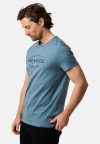 Niebieska bawełniana koszulka z okrągłym dekoltem, krótkimi rękawami oraz nadrukowanym graficznym motywem "Seaside" z przodu. Wzbogacona o metkę z logo u dołu.