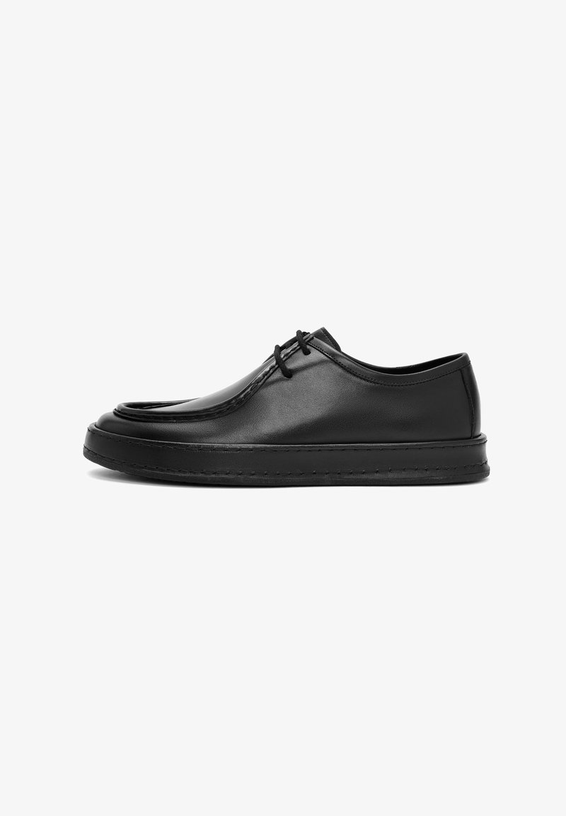 Zapatos de cuero negro con un acabado suave, punta redondeada, suela plana y diseño con cordones. Presenta costuras sutiles a lo largo de los bordes.