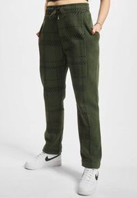 Grønne joggebukser med rutete mønster og to sidelommer. Har elastisk liv med snor. Kombinert med hvite joggesko.