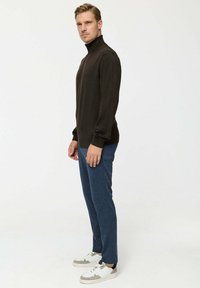 Sötétbarna garbópulóver, slim fit fazonban, kék nadrággal és fehér sportcipővel párosítva. Simább textúrával és minimalista dizájnnal rendelkezik.